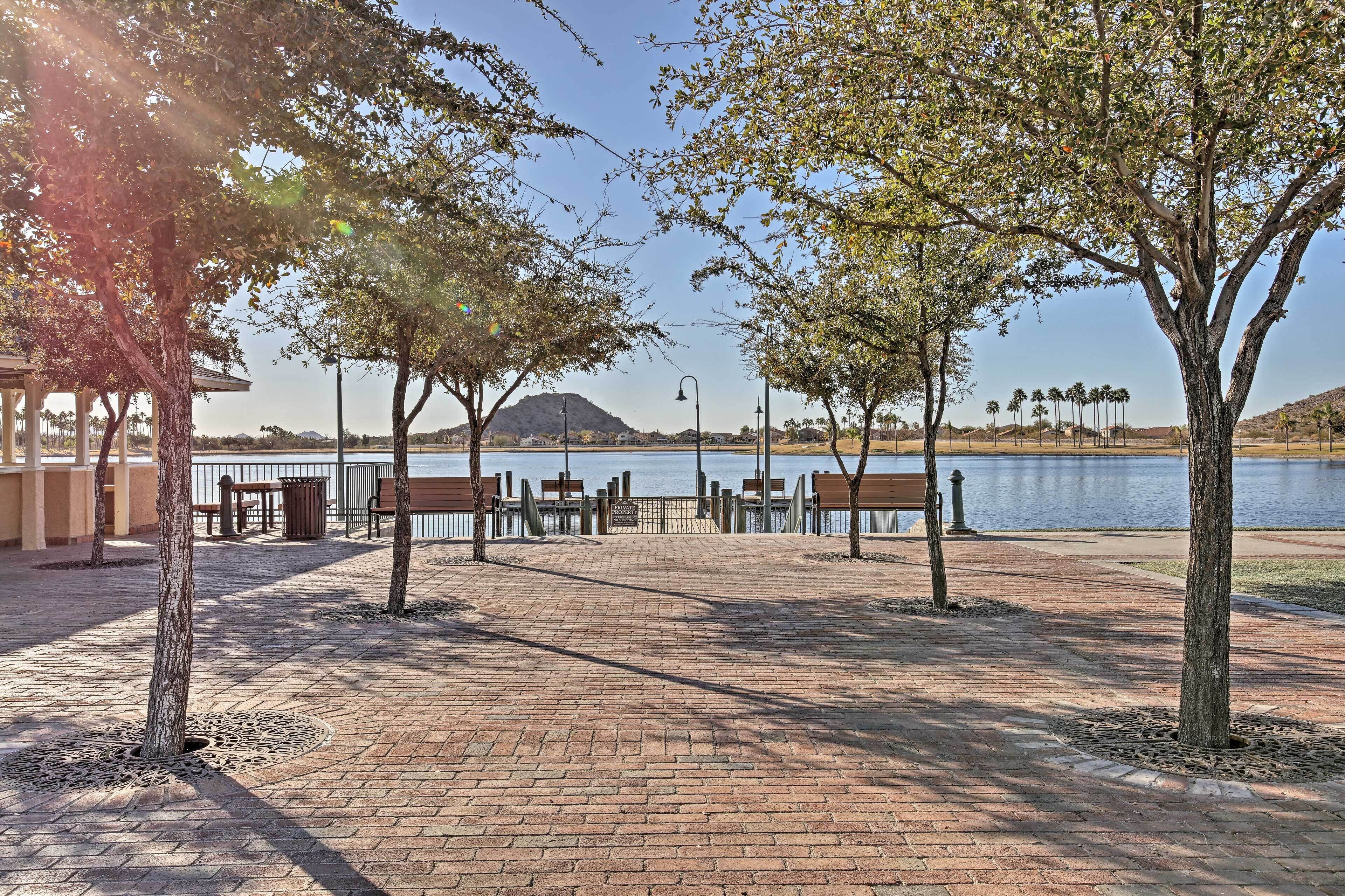 A paved walkway with benches and trees, leading to a body of water.