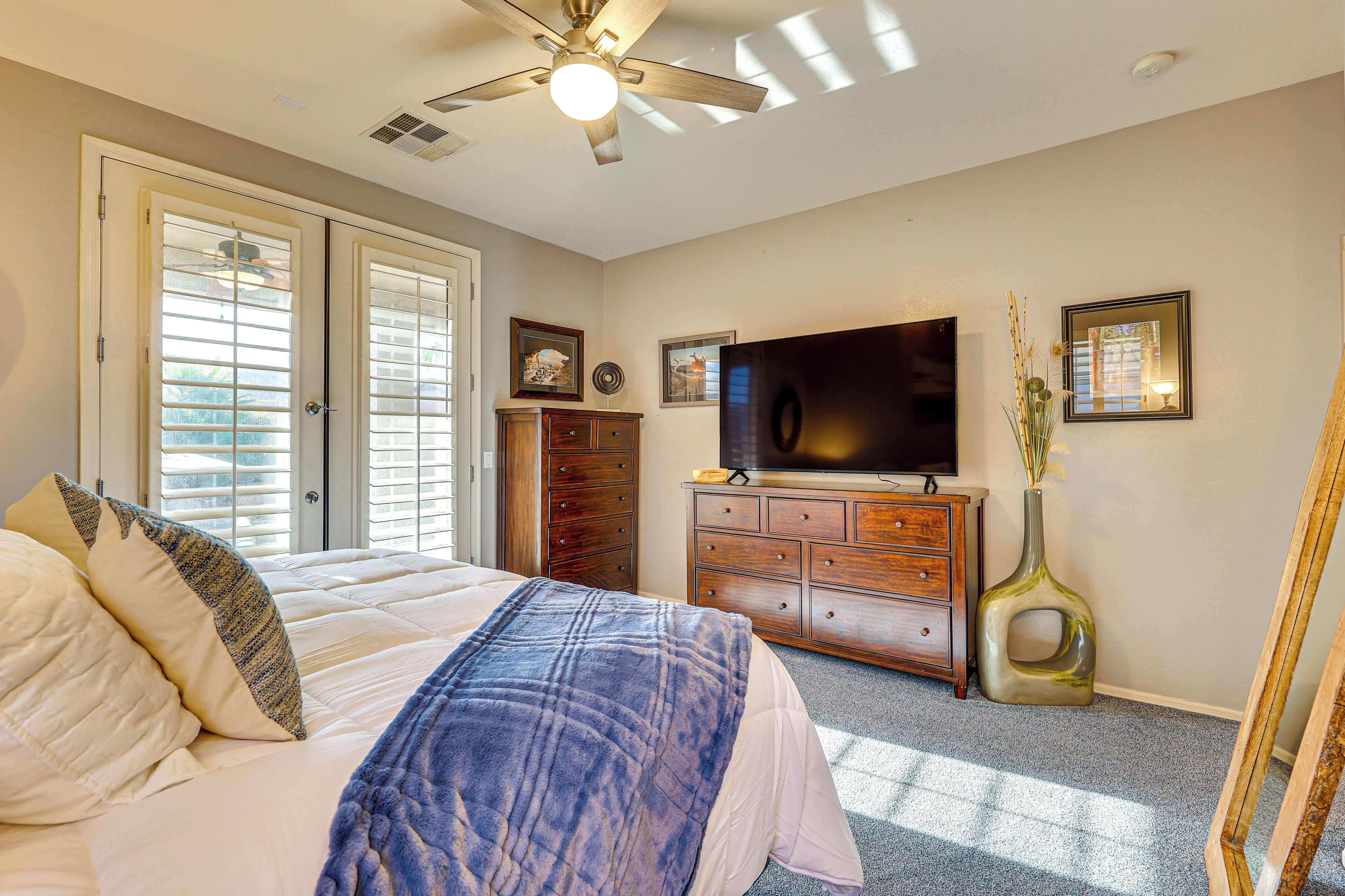 A bedroom with a bed, dresser, TV, and a ceiling fan.