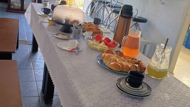 A dining table set with various food items and drinks, a coffee machine, and a window with curtains.