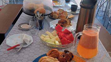 Uma mesa com diversos alimentos, um jarro de suco de laranja e um display de comida coberto.