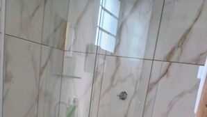 A bathroom with a toilet, a glass shower enclosure, and a marble wall.