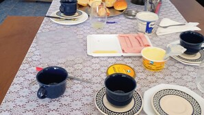 A dining table set with various dishes, utensils, and a coffee maker, indicating a meal setup in a room with a blue wall and a brown sofa.