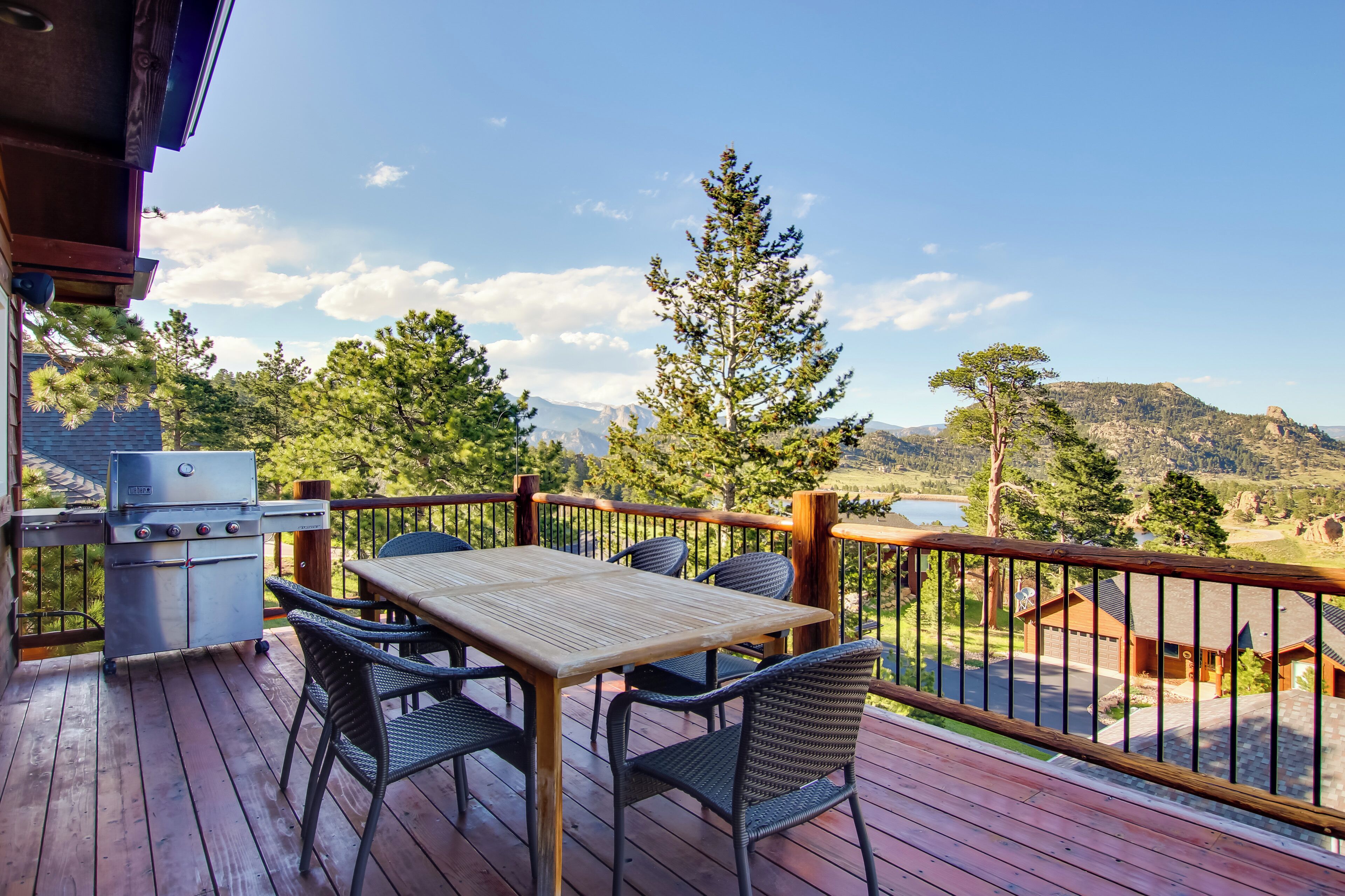 A wooden deck with a grill, table, and chairs, overlooking a mountainous landscape.
