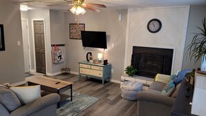 A living room with a ceiling fan, a fireplace, a television, and a clock on the wall. - ​Work Crew Special: Monthly Rates Full Kitchen & Laundry (Douglas)