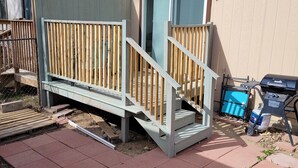 A wooden deck with a ramp leading to a door, a barbecue grill, and a blue container. - ​Work Crew Special: Monthly Rates Full Kitchen & Laundry (Douglas)