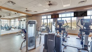 Une salle de sport équipée de divers appareils d’exercice, dotée de grandes fenêtres et d’un mur recouvert de miroirs.