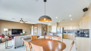 Une cuisine moderne avec des meubles en bois, un coin repas doté d’une table ronde et de chaises, un ventilateur de plafond et un éclairage encastré.
