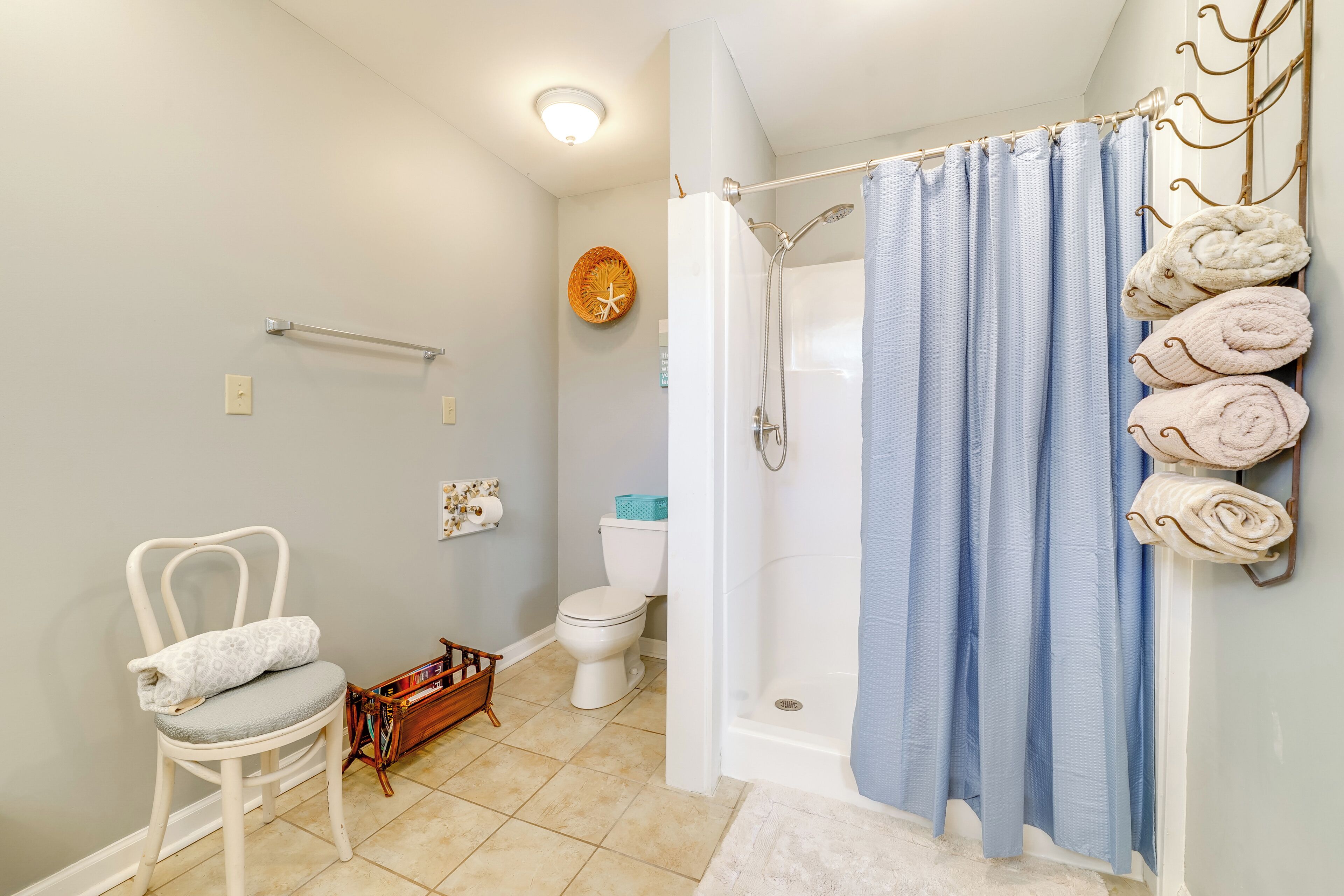 A bathroom with a shower, toilet, and a chair with a towel.