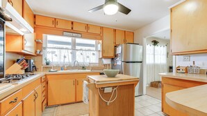 Una cocina con armarios de madera, una isla central, un refrigerador y una ventana con cortina.