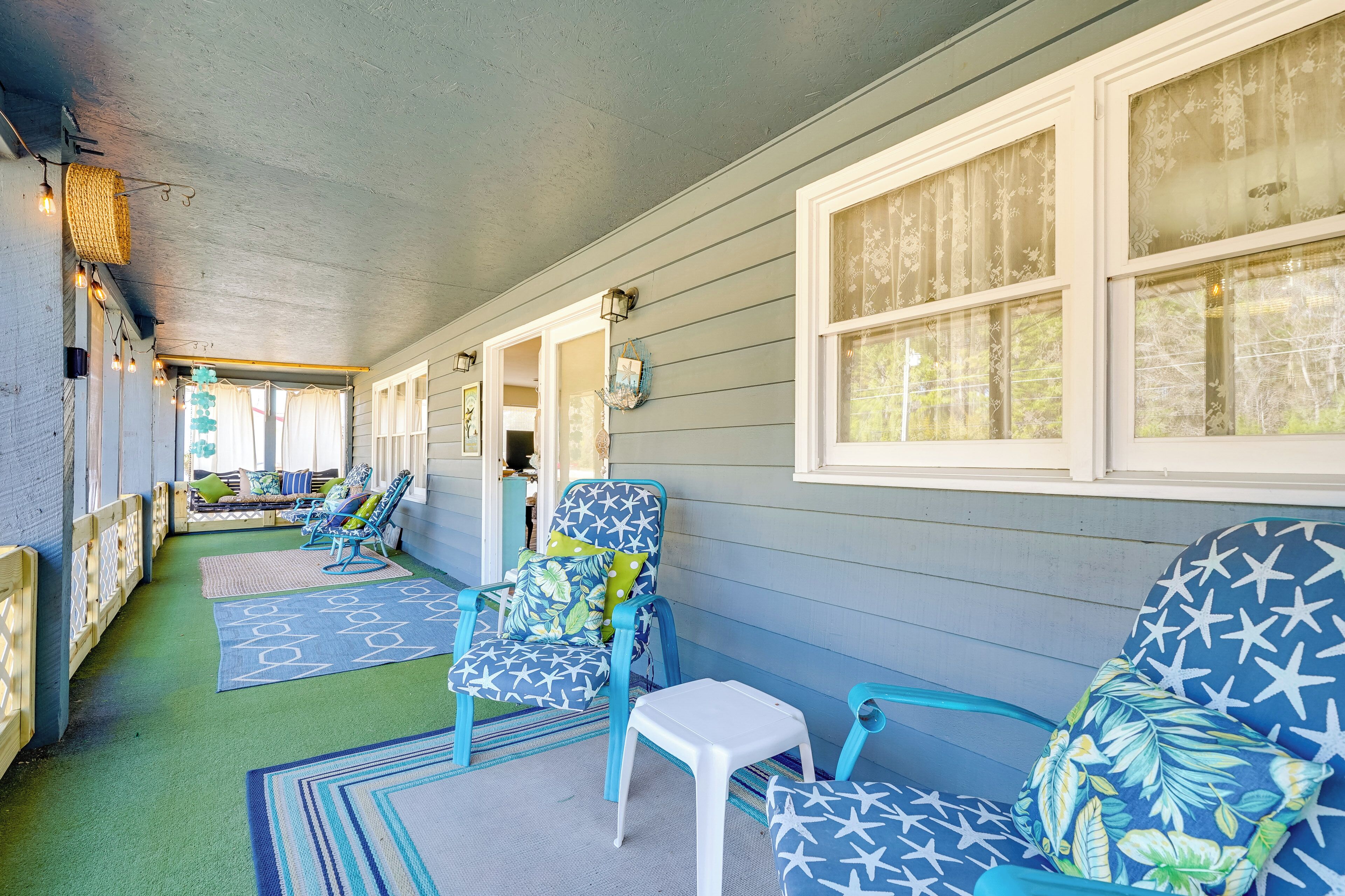A covered porch with blue and white patterned chairs, a small white table, and a green floor.