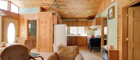 A spacious living area with a wooden ceiling, a ceiling fan, a dining table with chairs, and a kitchen area with wooden cabinets and appliances.