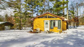 A yellow cabin with a brown roof, surrounded by snow and trees.