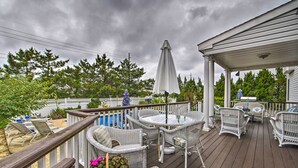 Une terrasse en bois avec des meubles en osier, un espace couvert et une vue sur une piscine et des arbres.