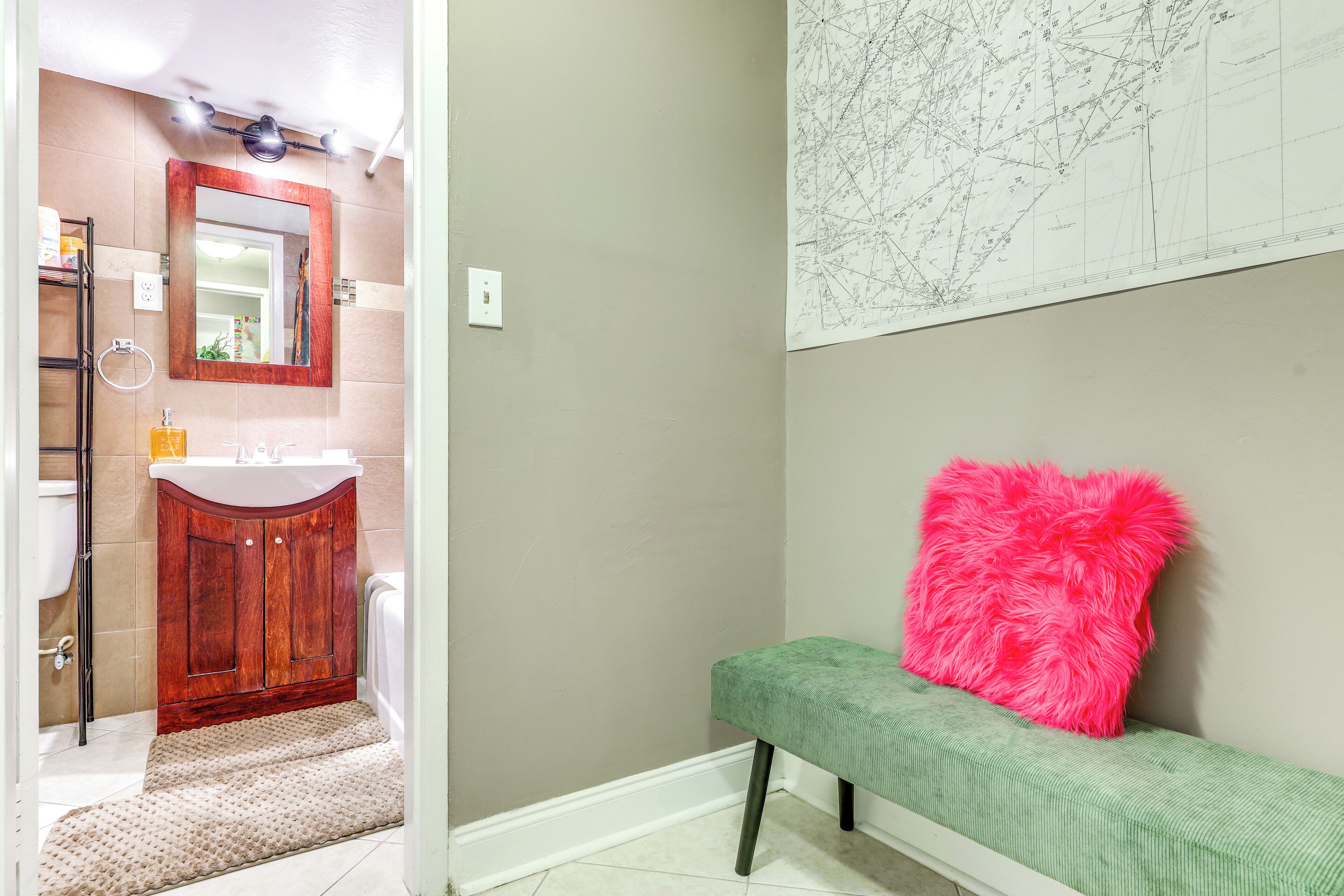 A bathroom with a wooden vanity, a mirror, and a green bench with a pink pillow.