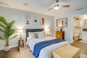 A modern bedroom with a bed, bedside tables, a ceiling fan, and a bathroom visible through an open door. - 7 Mi to River District: Cape Coral Home w/ Lanai (Cape Coral)