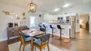 A modern kitchen with white cabinets, a stainless steel refrigerator, and a coffee machine. There is a dining area with a table and chairs, and a bar with stools. - 7 Mi to River District: Cape Coral Home w/ Lanai (Cape Coral)