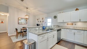A modern kitchen with white cabinets, granite countertops, and a dining area with wooden chairs. - 7 Mi to River District: Cape Coral Home w/ Lanai (Cape Coral)