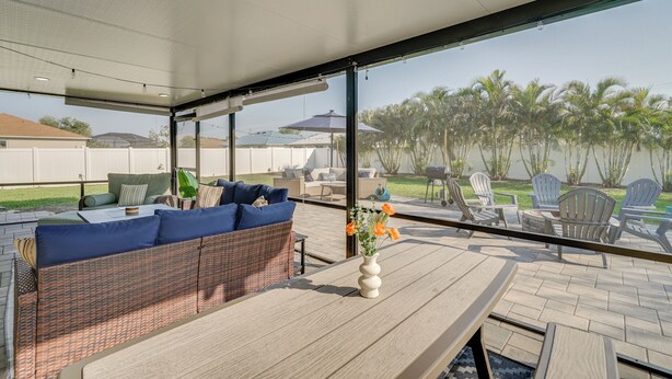 An outdoor patio with wicker furniture, a wooden table, and a vase of flowers. - 7 Mi to River District: Cape Coral Home w/ Lanai (Cape Coral)