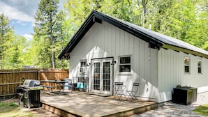 Une cabane blanche dotée d’une terrasse, d’un barbecue et d’une table de pique-nique.