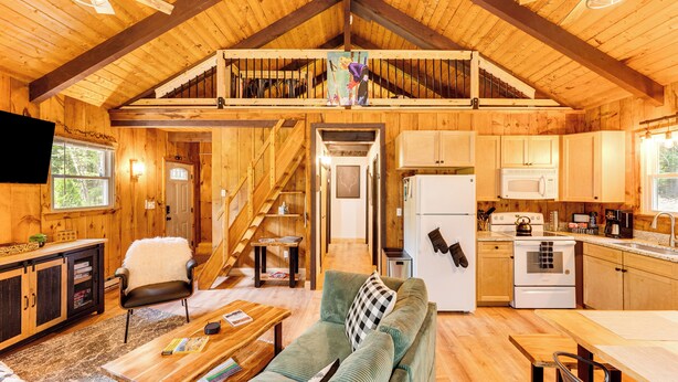 Un chalet rustique en bois doté d’une chambre à coucher en mezzanine, d’une cuisine avec des appareils électroménagers d’époque et d’un salon confortable avec un canapé et une table basse.