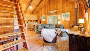 L’intérieur d’une cabane en bois comprend une chambre à coucher située en mezzanine, un coin repas et un salon avec une cheminée.