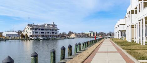 A waterfront promenade with a row of buildings, a clear sky, and a calm water body.