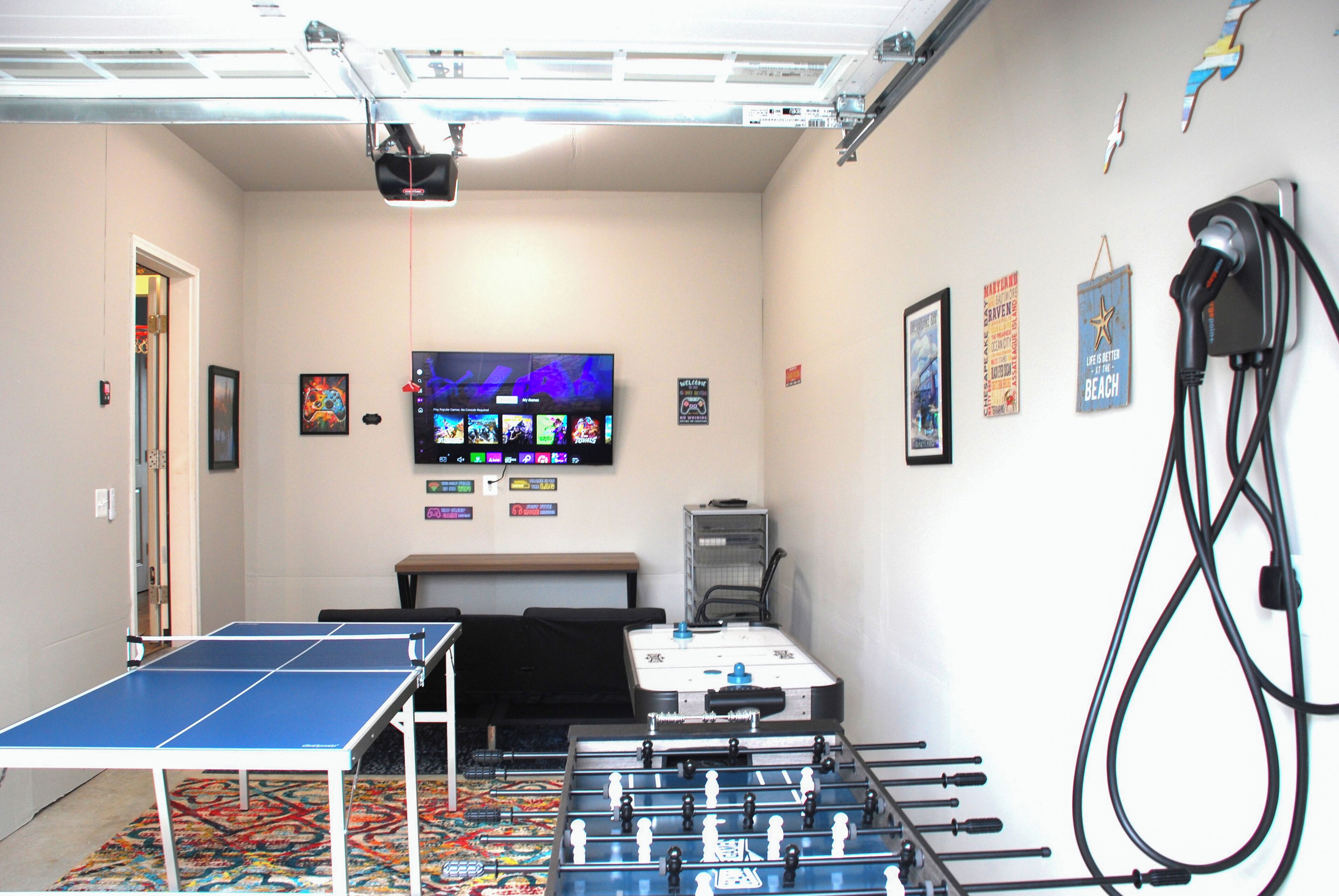 A room with a ping pong table, foosball table, and a television mounted on the wall.