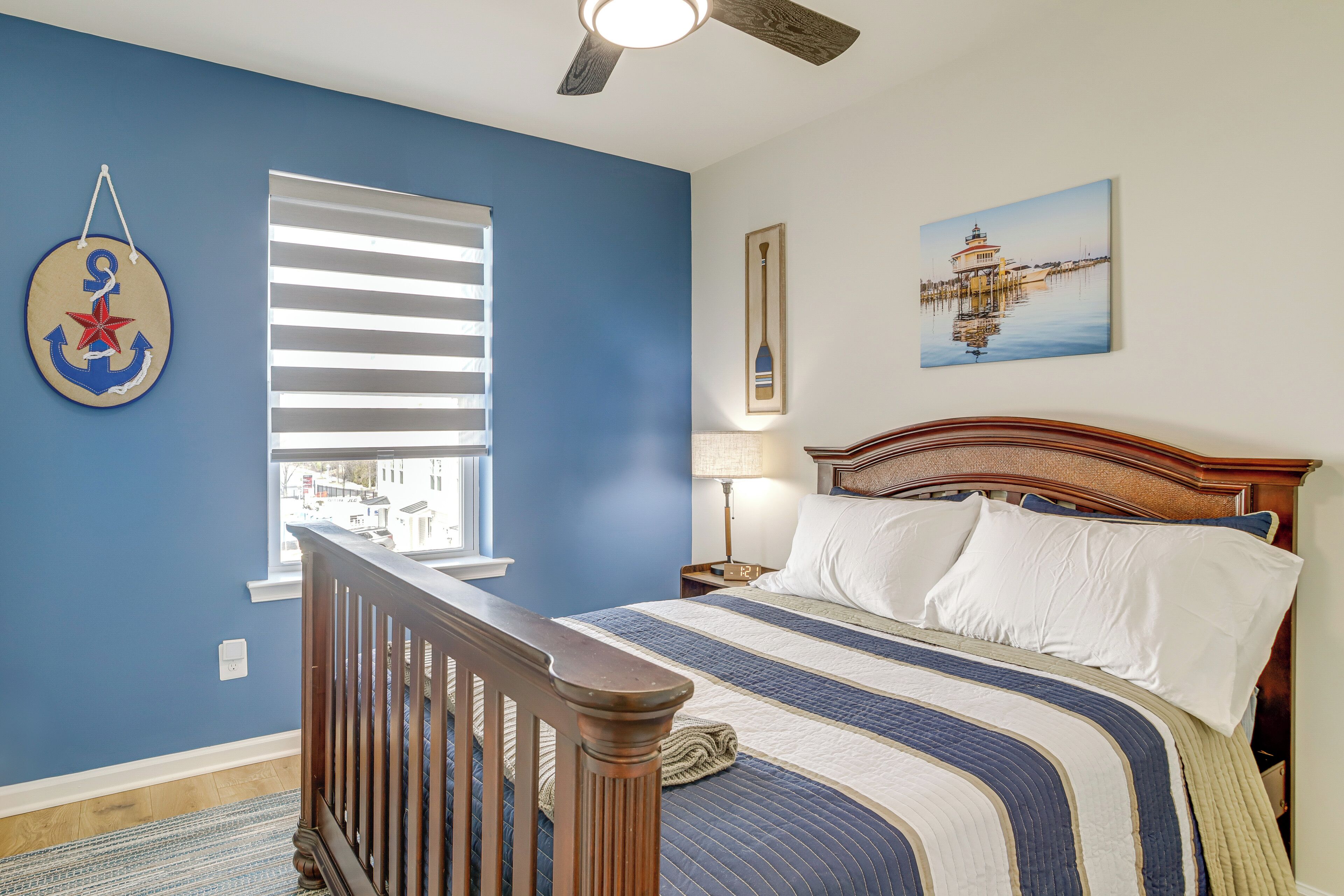 A bedroom with a bed, a window with blinds, a ceiling fan, a lamp, and a painting on the wall.