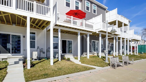 A multi-story residential building with a covered porch and a red umbrella. - Walk to Dtwn: Waterfront Eastern Shore Townhome! (Cambridge)