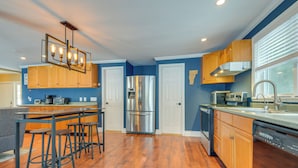 A modern kitchen with wooden cabinets, a stainless steel refrigerator, and a bar area with stools.