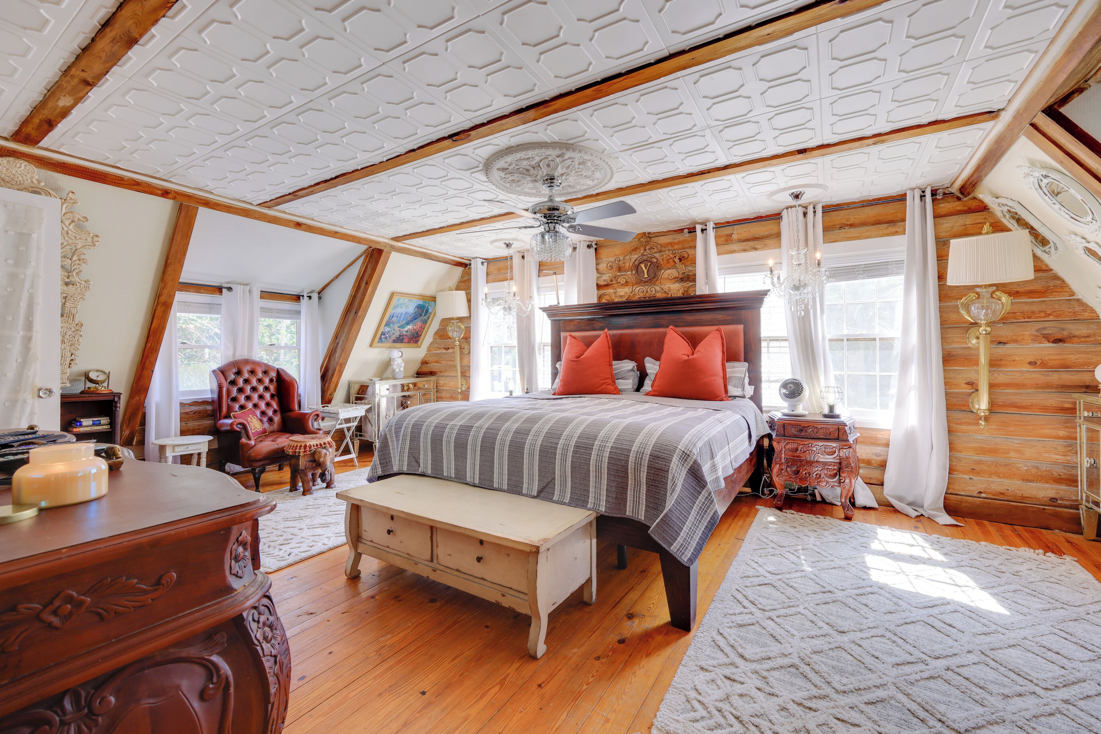 A bedroom with a large bed, wooden ceiling, and a chandelier.