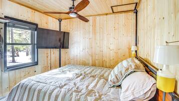 A wooden-paneled room with a bed, a ceiling fan, a window, and a TV mounted on the wall.