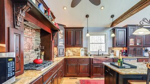 A kitchen with dark wooden cabinets, a stone backsplash, and a red rug. - Large Deck: Luxe 6-acre Retreat in Dahlonega! (Dahlonega)