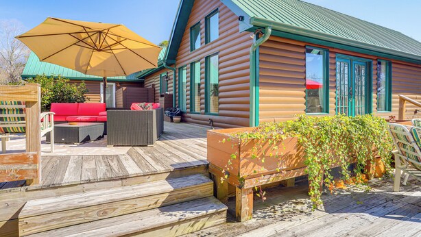 A log cabin with a wooden deck, outdoor seating, and a large umbrella. - Large Deck: Luxe 6-acre Retreat in Dahlonega! (Dahlonega)