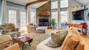 A spacious living room with a fireplace, large windows, and a television. - Large Deck: Luxe 6-acre Retreat in Dahlonega! (Dahlonega)