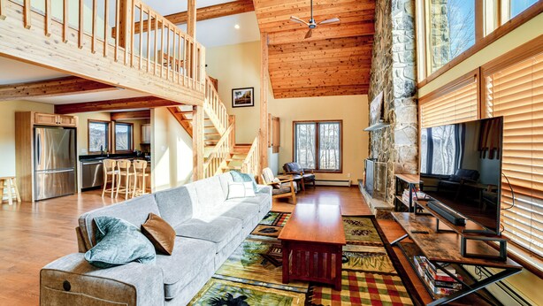 A spacious living area with a high ceiling, wooden beams, a built-in fireplace, a large sofa, and a dining table. - Golf, Fish & Ski: Retreat w/ Game Room in Thompson (Thompson)