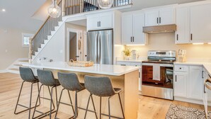 A modern kitchen with a central island, stainless steel appliances, and a staircase leading to an upper level. - Dock & Game Room: New Waterfront Home in Lyman! (Alfred)