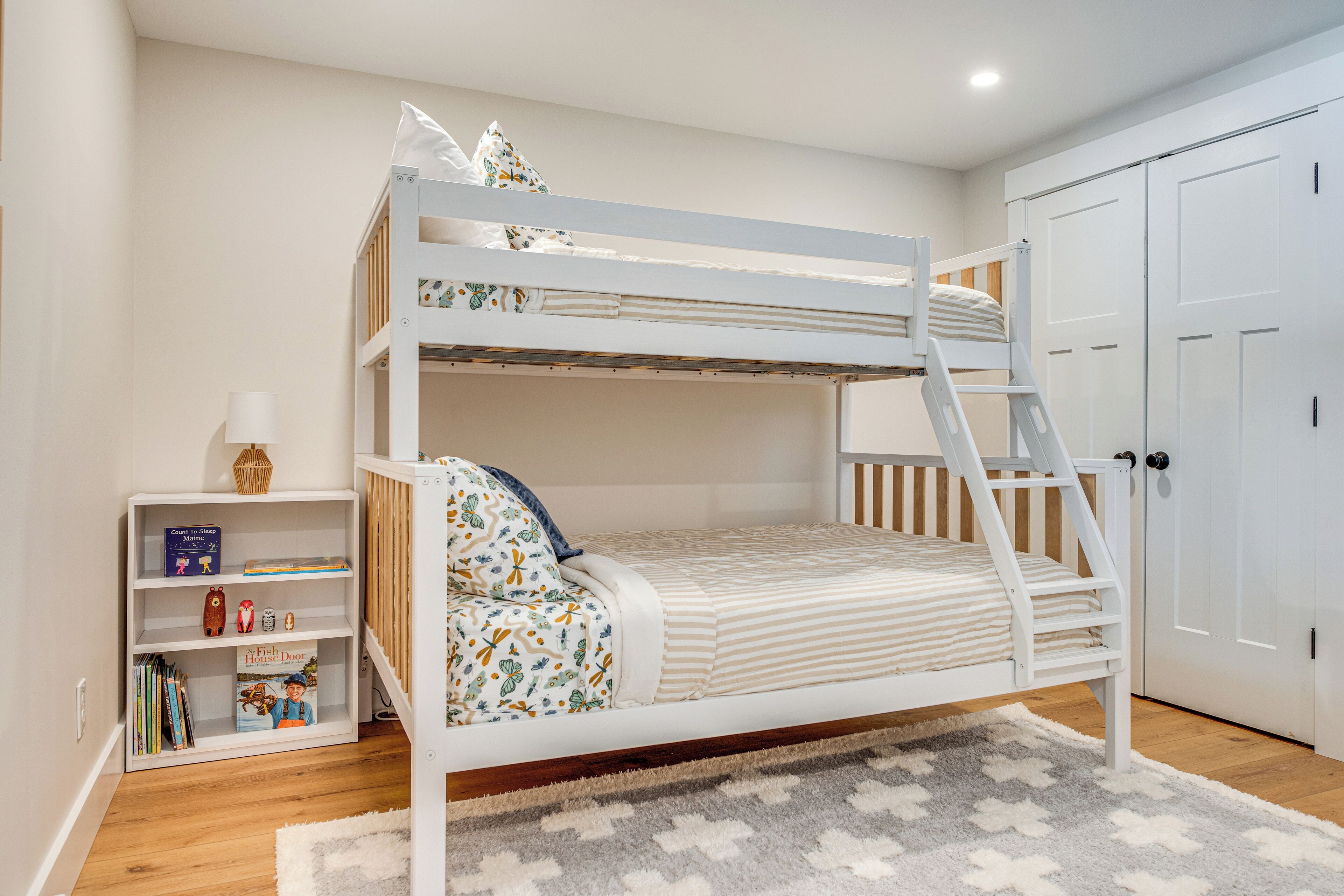 A bunk bed with a ladder, a bookshelf with books, and a door in a bedroom.