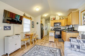 A compact kitchen with wooden cabinets, a microwave, and a stove. There is a dining area with a table and chairs, and a television mounted on the wall. - Remote Workers Welcome: Tiny Home in Port Angeles! (Port Angeles)