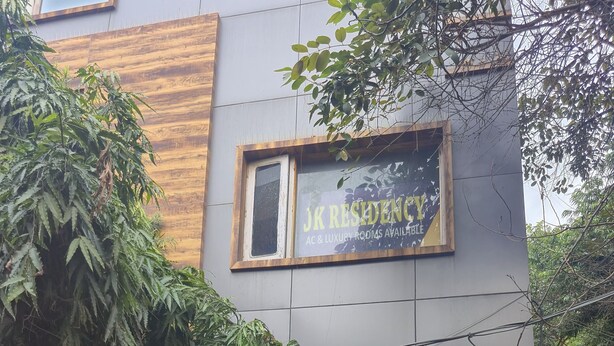 Ein Gebäude mit einem Schild, auf dem „JK Residency“ steht und Klimaanlage und luxuriöse Zimmer beworben werden.