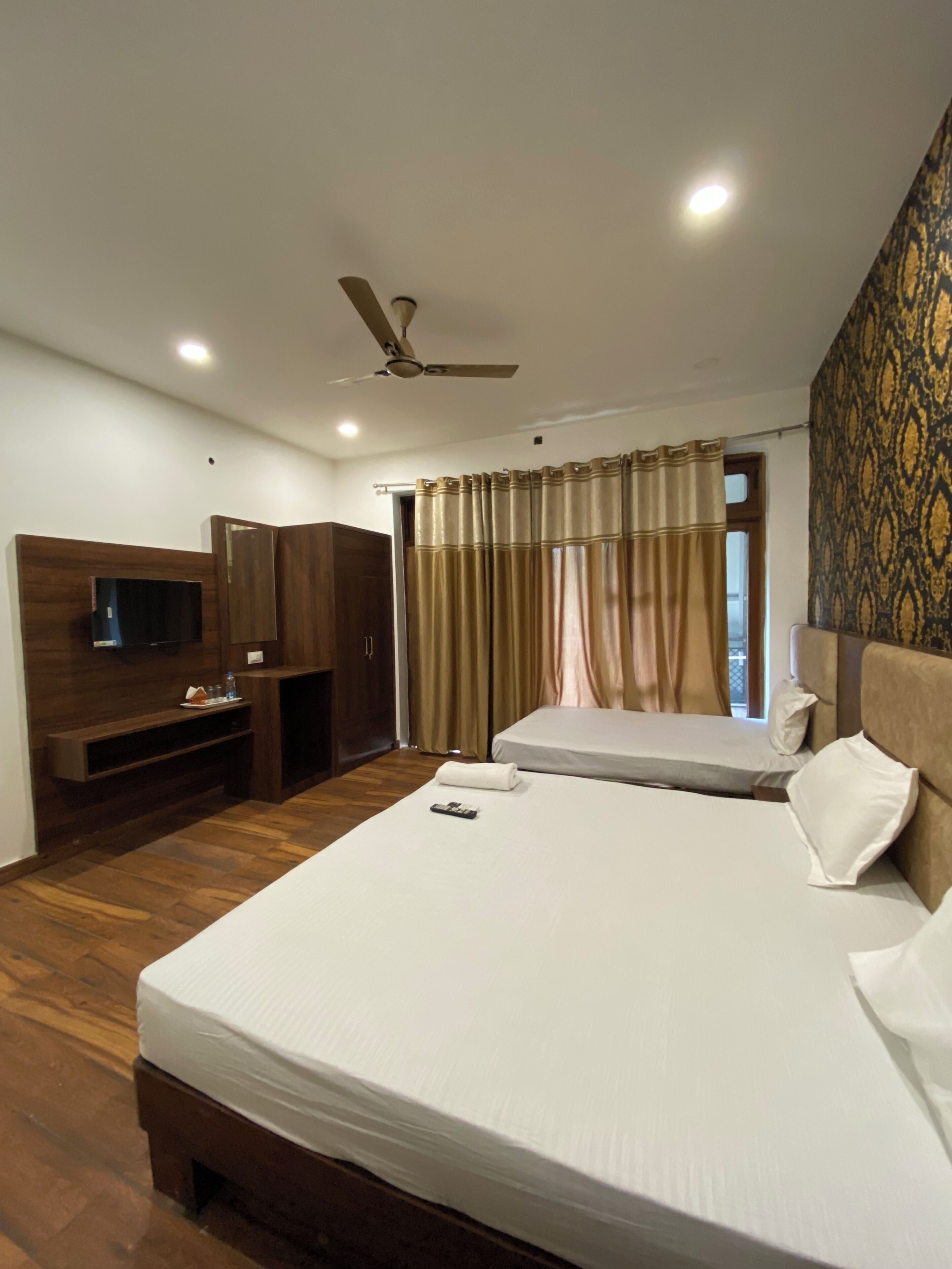 A hotel room with a bed, a TV, a desk, and a ceiling fan.