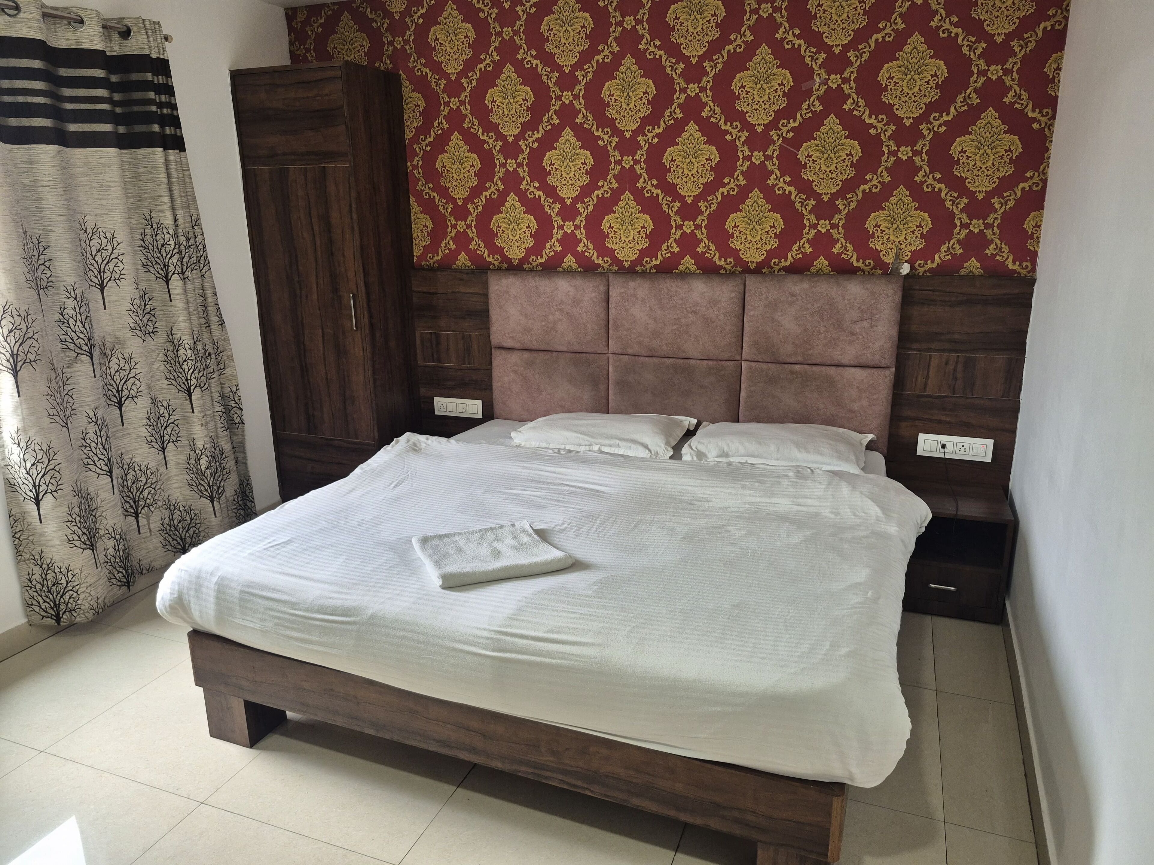 A bedroom with a wooden bed, a headboard, a wardrobe, and patterned curtains.