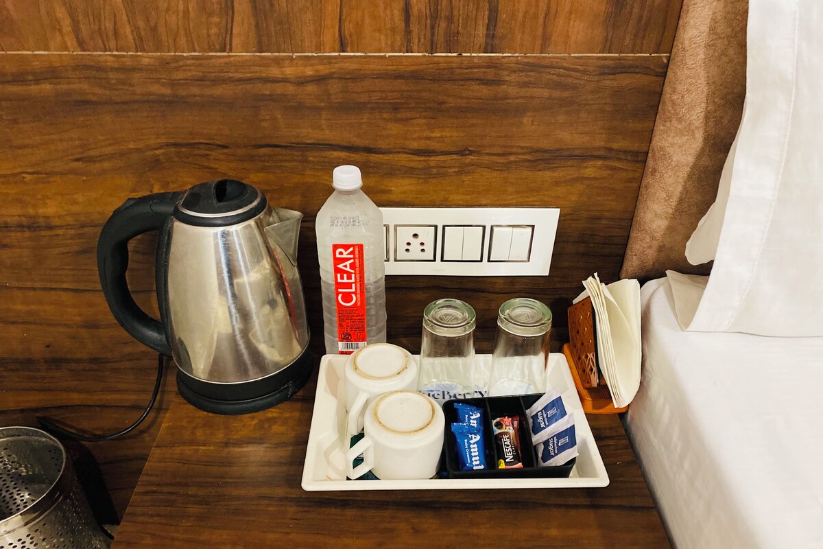 Ein ordentlich eingerichtetes Hotelzimmer mit Wasserkocher, Tablett mit Kaffeetassen, Zuckerportionen und einer Wasserflasche auf dem Nachttisch.