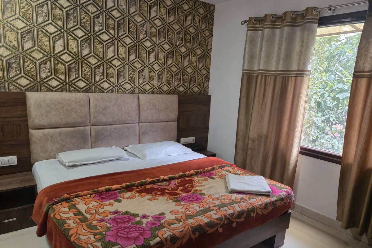 A neatly made bed with a floral bedspread, a headboard, and a window with curtains.