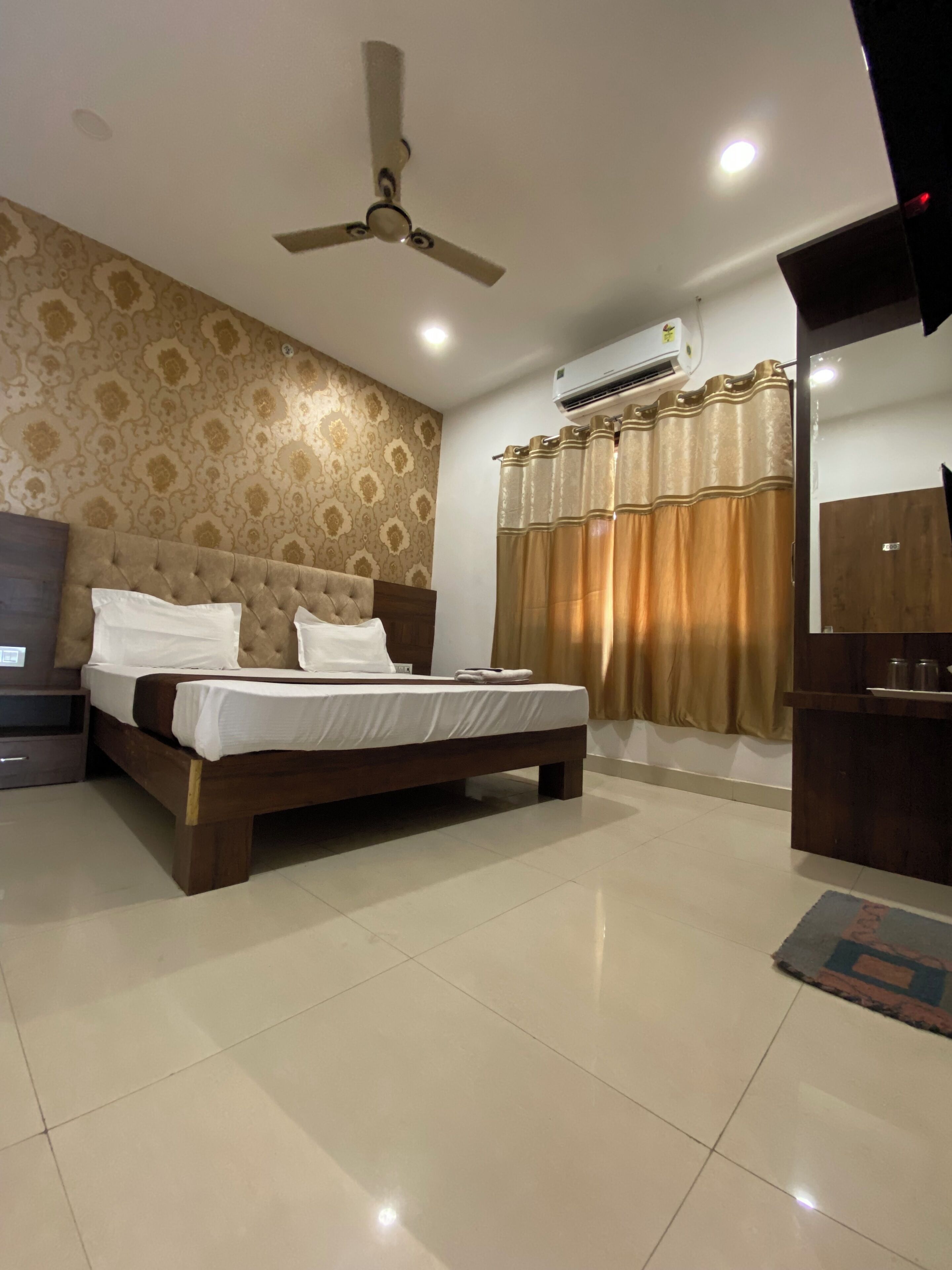 A bedroom with a bed, a ceiling fan, an air conditioning unit, a wooden wardrobe, and a bathroom with a shower curtain.