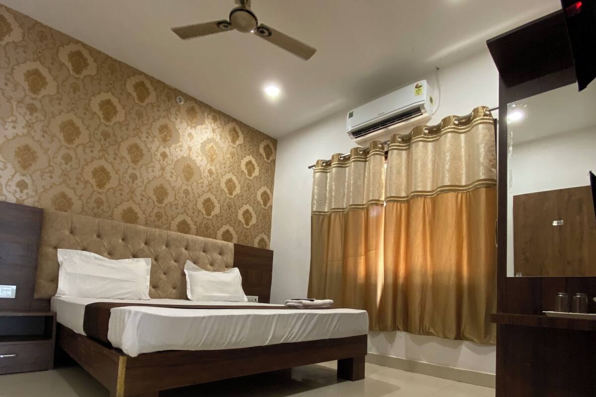 A bedroom with a bed, a ceiling fan, an air conditioning unit, a wooden wardrobe, and a bathroom with a shower curtain.