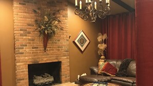 Un salon chaleureux avec une cheminée en briques, un canapé en cuir, une table basse et un lustre.