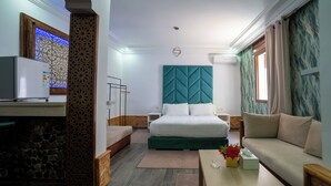 A modern hotel room with a bed, a sofa, a small table, a nightstand, a decorative wall panel, and a window with curtains. - DAR BLANCA (Chefchaouen)