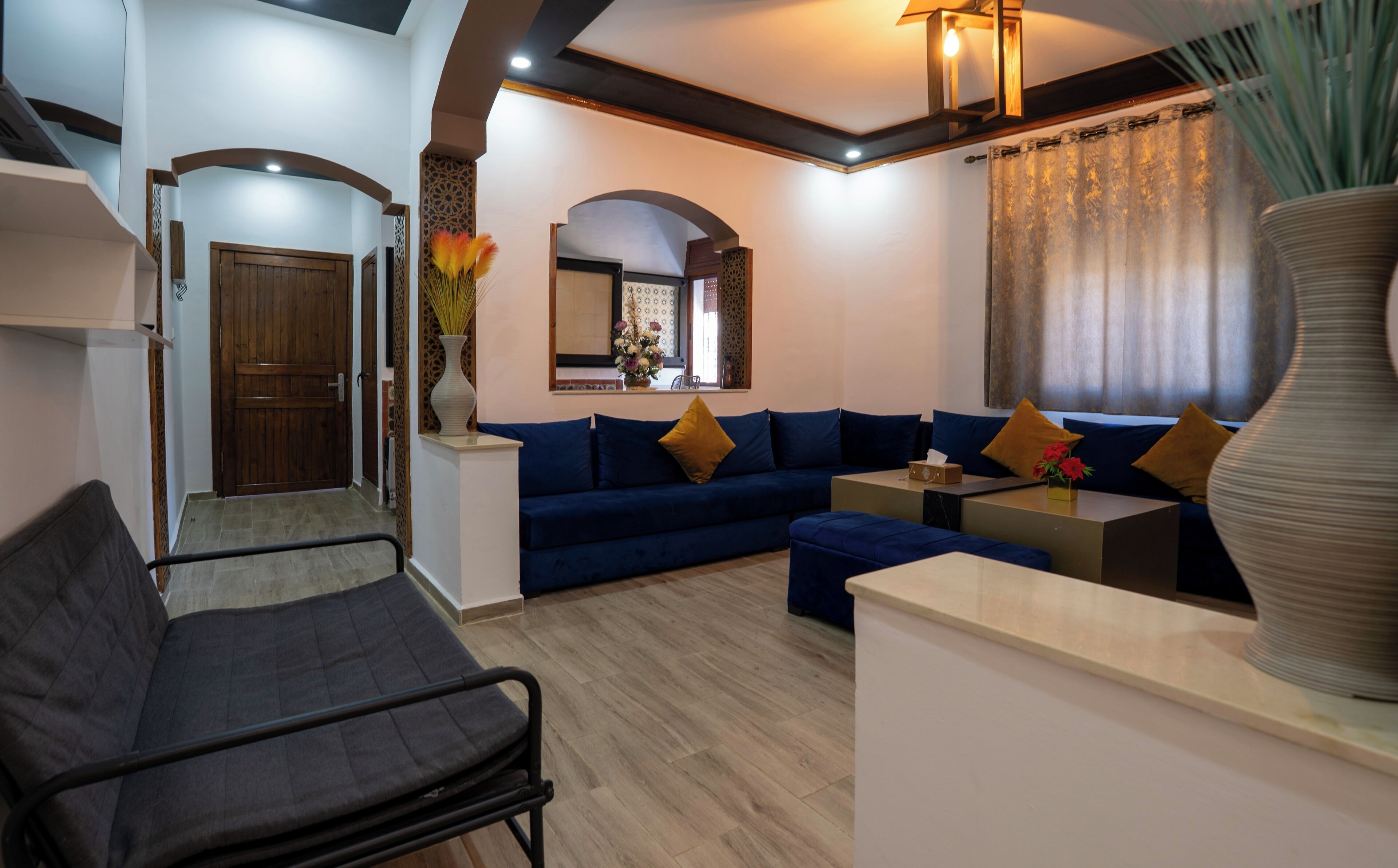 Una sala de estar moderna con un sofá, una mesa de centro y un sillón. Hay una puerta de madera y un espejo en la pared.