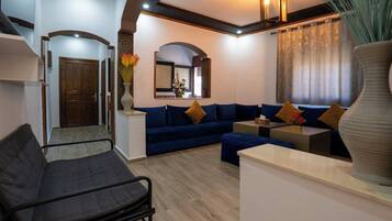 Una sala de estar moderna con un sofá, una mesa de centro y un sillón. Hay una puerta de madera y un espejo en la pared.